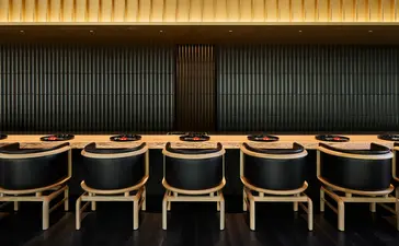 Taka-An dining venue at Aman Kyoto, wooden chairs arranged at counter with golden wall panels.