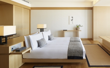 Deluxe room at Aman Tokyo featuring a bed with white linens, wooden furnishings, and warm neutral tones.