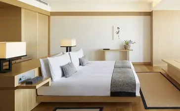 Deluxe Room at Aman Tokyo with a low-profile bed dressed in white linens, warm wood panelling, and minimalist furnishings.