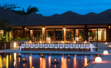 West Villa clubhouse at Amanpulo with dining area overlooking illuminated pool at dusk.