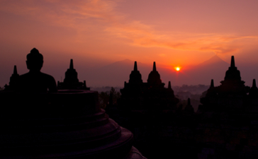 Silhouettes of Borobudur temple spires against an orange and pink sunrise sky at Amanjiwo resort.