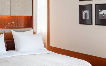 Principal bedroom at Aman Sveti Stefan with sea views, featuring wooden-framed bed and suede ottoman.
