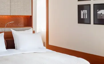Principal bedroom at Aman Sveti Stefan with sea views, featuring wooden-framed bed and suede ottoman.