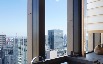 Aman Tokyo suite with floor-to-ceiling window framing Tokyo's skyline and a sleek black soaking tub.