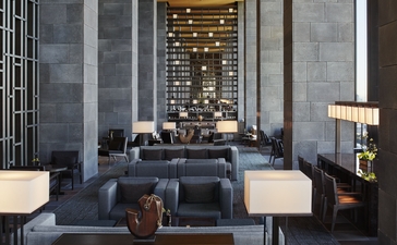 Lounge area at Aman Tokyo with high ceilings, dark furnishings, and illuminated shelving.