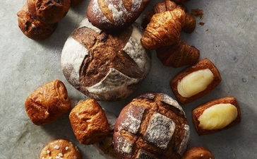 Assorted freshly baked pastries and bread from Aman Tokyo's patisserie, arranged on a grey surface.
