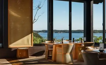 Dining space at Amanemu resort with wooden furniture and expansive views over water and landscape.