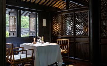 法云安缦度假村的餐厅内部，设有铺着蓝色桌布的餐桌、木制椅子和传统装饰元素。