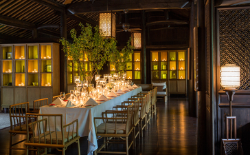 Wedding setup at Amanfayun with candlelit long dining table beneath wooden beams and warm lighting.