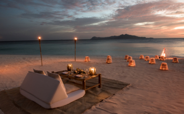 Beach barbecue setup at Amanpulo with dining table and lanterns at sunset.