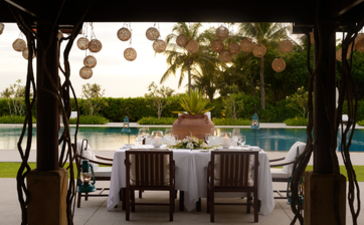 Covered dining pavilion at Amanpulo with poolside seating and tropical gardens beyond.