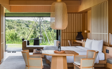 Suite at Amanemu resort with wooden interior, dining table, and views towards gardens.