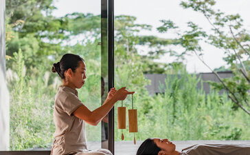 Wellness practitioner guides a guest through a massage session overlooking verdant gardens at Amanemu resort.