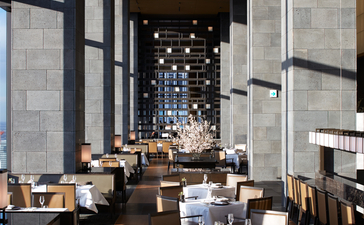 Arva dining venue at Aman Tokyo, featuring soaring concrete columns and warm lighting, with tables set for service.