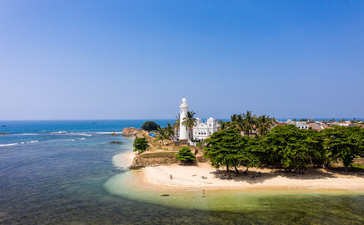 Aerial view of Amangalla's lighthouse on a sandy peninsula surrounded by turquoise waters and tropical vegetation.