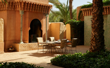 Garden suite courtyard at Amanjena with terracotta walls, wooden seating, and palm trees.
