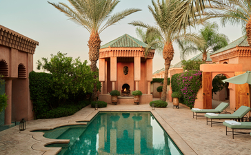 Al Hamra Maison at Amanjena, a terracotta-coloured villa with a reflecting pool and palm trees in a Marrakech riad setting.