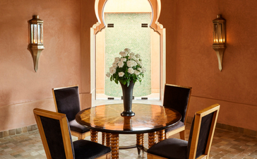 Al Hamra Maison dining area at Amanjena with round table, chairs, and fresh flowers.
