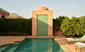 Pavilion with green door reflected in swimming pool at Amanjena, surrounded by hedging and terracotta architecture.