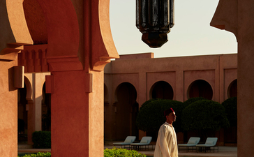 安缦珍纳度假村中庭，红土拱门框景，水池倒映，穿白衣女性漫步其中。