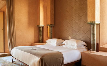 安缦珍纳度假村的宽敞principal卧室，配有铜色床框、白色床上用品和温暖的土色调装饰。