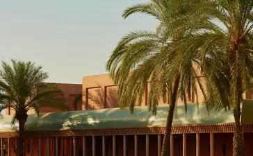 Palmiers bordant un canal à Amanjena, resort au Maroc, avec bâtiment en terre cuite en arrière-plan.
