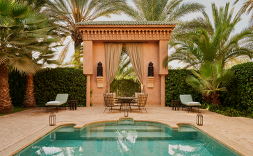Courtyard with turquoise plunge pool at Amanjena, framed by terracotta arches and palm trees.