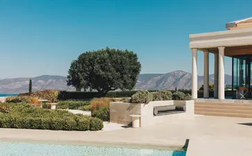 Amanzoe property overlooking terraced gardens and distant mountains, with a mature tree and swimming pool in the foreground.