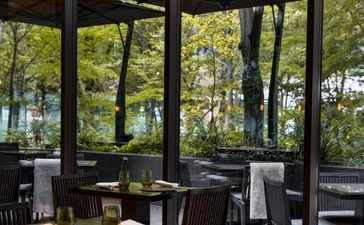 Ben Richards' photograph of the café at Aman Tokyo hotel, showing dining tables by floor-to-ceiling windows overlooking trees.