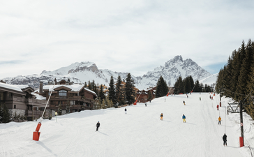 Skiers and snowboarders on snow-covered slopes at Aman Le Mélézin, with snow-capped mountains in the distance.