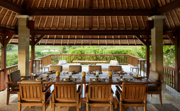 Dining pavilion at Aman Villas at Nusa Dua with wooden furnishings and garden views.