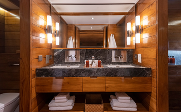 Amandira deluxe cabin bathroom with dual vanity, warm wooden cabinetry, and brass wall sconces.
