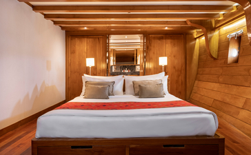 Deluxe cabin bedroom at Amandira with wooden walls, warm lighting, and a bed dressed in white linens with an orange throw.