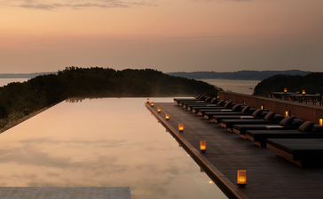 Amanemu's main pool at dusk, reflecting warm light across still water with forested shoreline beyond.