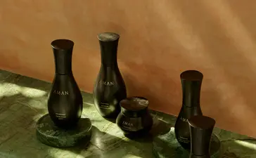 Quatre bougies parfumées noires Aman Skincare alignées sur une surface blanche à Amanjena, la station balnéaire de Marrakech.