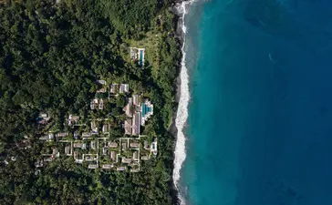アマンキラ リゾートの海岸線を上空から望むドローン写真。紺碧の海と緑生い茂る海岸が隣り合う。
