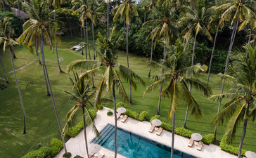 Aerial view of Amankila resort's swimming pool surrounded by palm trees and manicured gardens in Indonesia.