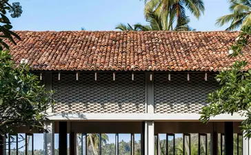 Pavilion with terracotta roof at Amanwella, framed by palm trees and tropical foliage.