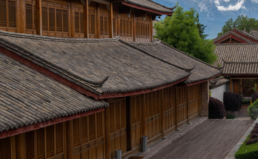 Monk in red robes walking across wooden deck at Amandayan, with traditional architecture and snow-capped mountains beyond.