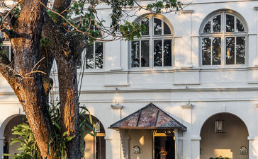 Two guests sit beneath a large tree outside Amangalla's white colonial facade.