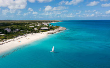 Plage de sable blanc d'Amanyara avec voilier en eau turquoise, vue aérienne.