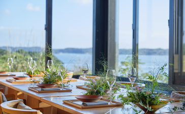 Amanemu dining venue with floor-to-ceiling windows overlooking coastal waters and gardens.