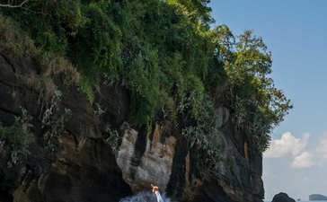 Woman in white standing by traditional wooden boat on sandy beach at Amankila resort.