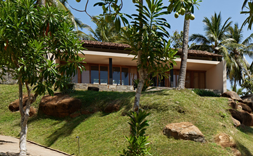 Amanwella garden with pavilion-style buildings nestled amongst lush tropical vegetation and mature palms.