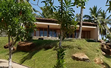 Amanwella garden with pavilion-style buildings nestled amongst lush tropical vegetation and mature palms.