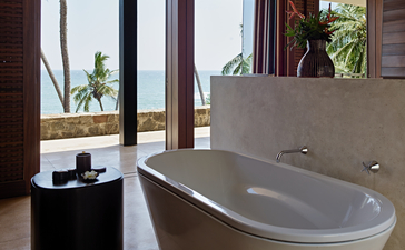 Amanwella suite bathtub with ocean views through open doors to tropical gardens.