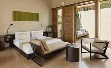 Amanwella suite bedroom with white bed, green artwork, wooden furniture and sliding doors opening to terrace.