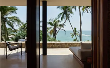 Suite with ocean view at Amanwella, Sri Lanka, showing open doors to a terrace with seating and palm trees.