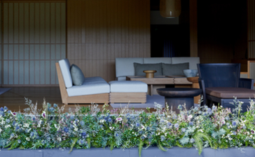 Wooden bench and low tables on a wooden deck at Amanemu, with flowering plants in the foreground.