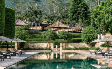 Amanjiwo's pool terrace overlooking lush grounds and stone architecture nestled among tropical vegetation.